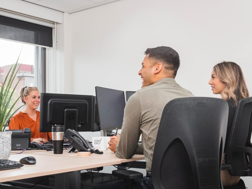 Drie collega's zitten op kantoor te lachen achter hun scherm